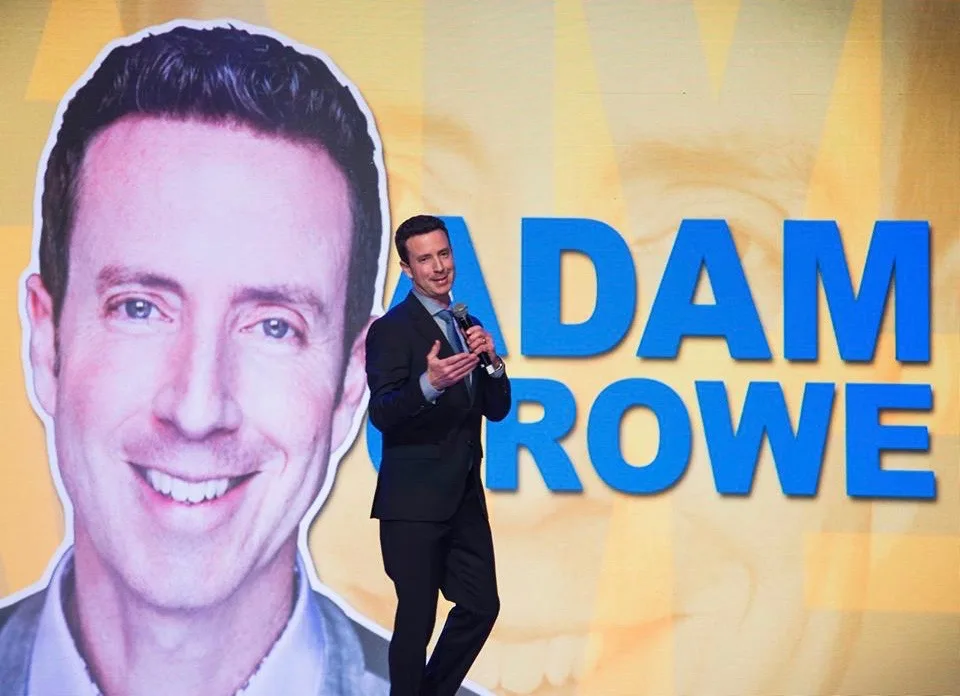 Adam Growe performing comedy in front of a branded stage screen
